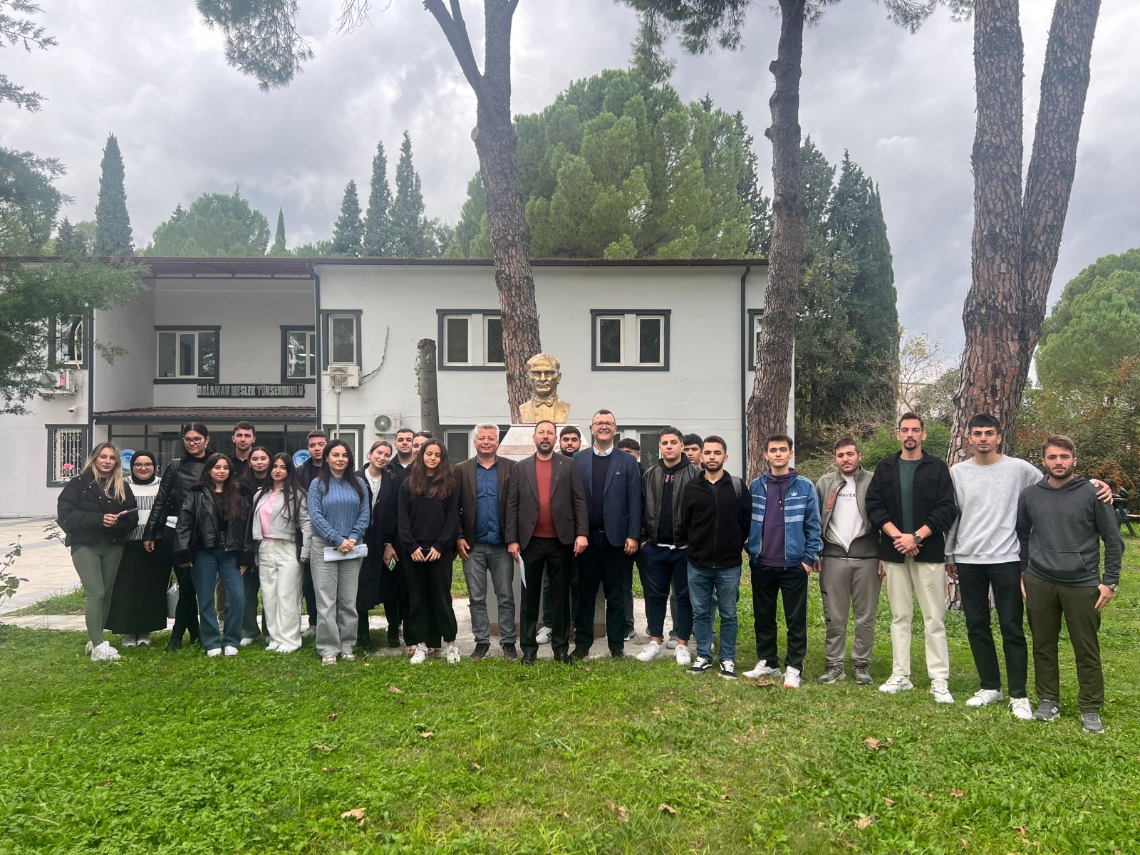 Dalaman MYO’da geniş ve aydınlık bir sınıfta düzenlenen konferans. Öğrenciler sıralarda oturarak konuşmacıyı dikkatle dinliyor. Sınıfın ön kısmında ayakta duran bir öğretim elemanı öğrencilere hitap ediyor. Pencerelerden doğal ışık içeri giriyor; sınıf kalabalık ve düzenli.